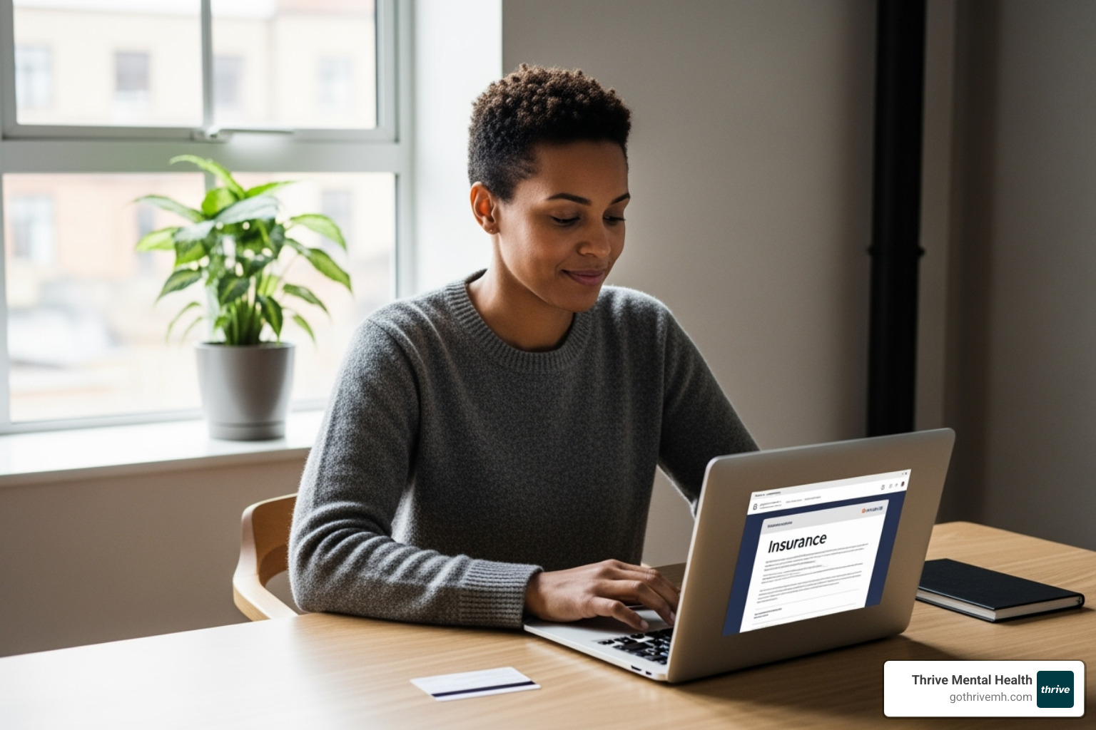 Person on a laptop with an insurance card next to it, looking up benefits. - online iop program