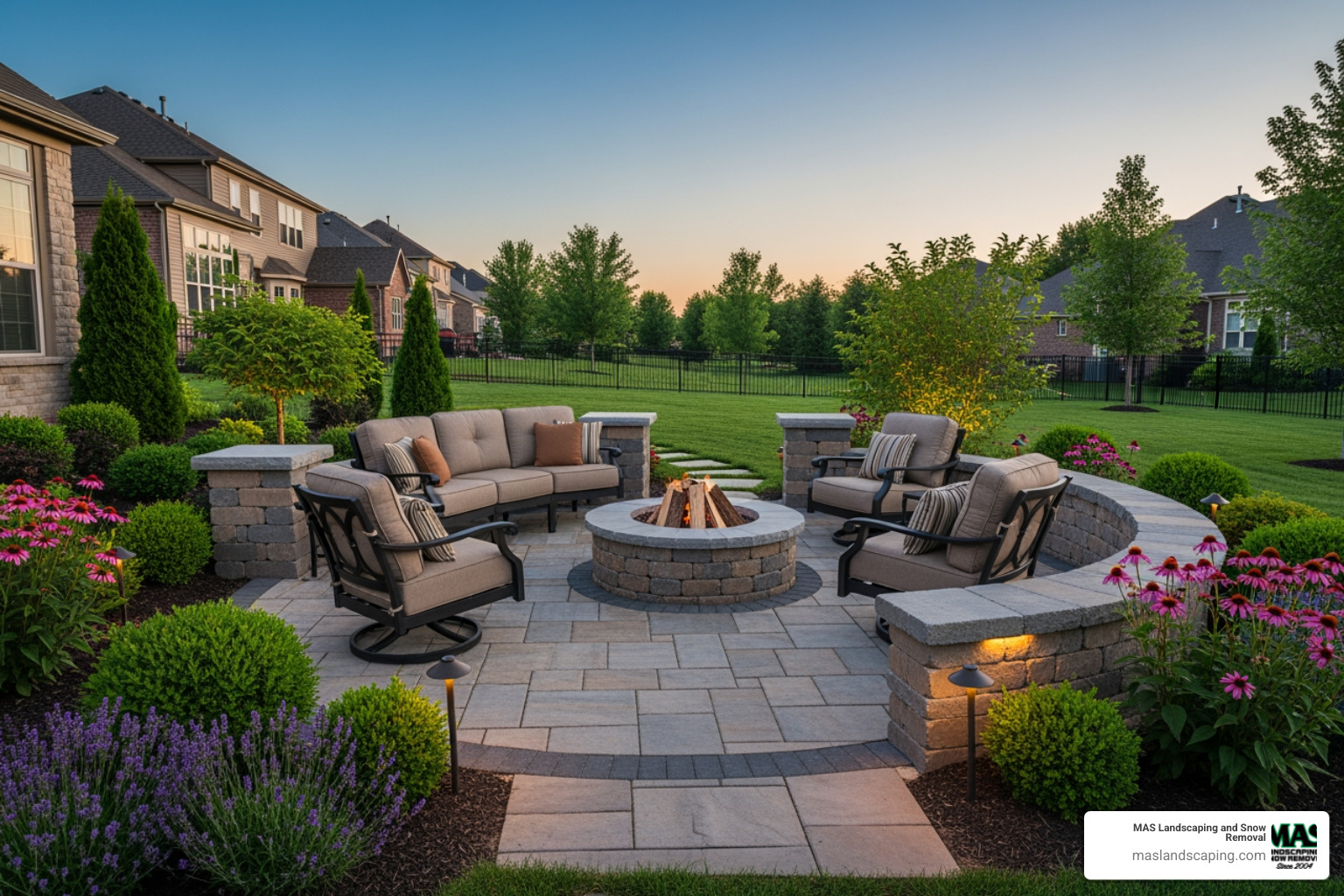 A custom stone patio with a built-in fire pit, surrounded by comfortable seating in a Saugus backyard - Landscape Construction Saugus MA
