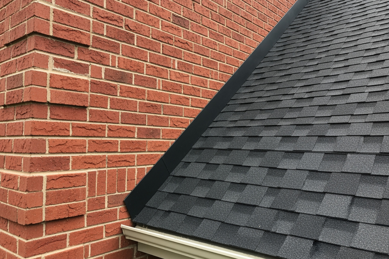 Close-up showing the sharp contrast between red brick texture and dark architectural shingles - black shingles on red brick Close-up showing the sharp contrast between red brick texture and dark architectural shingles - black shingles on red brick