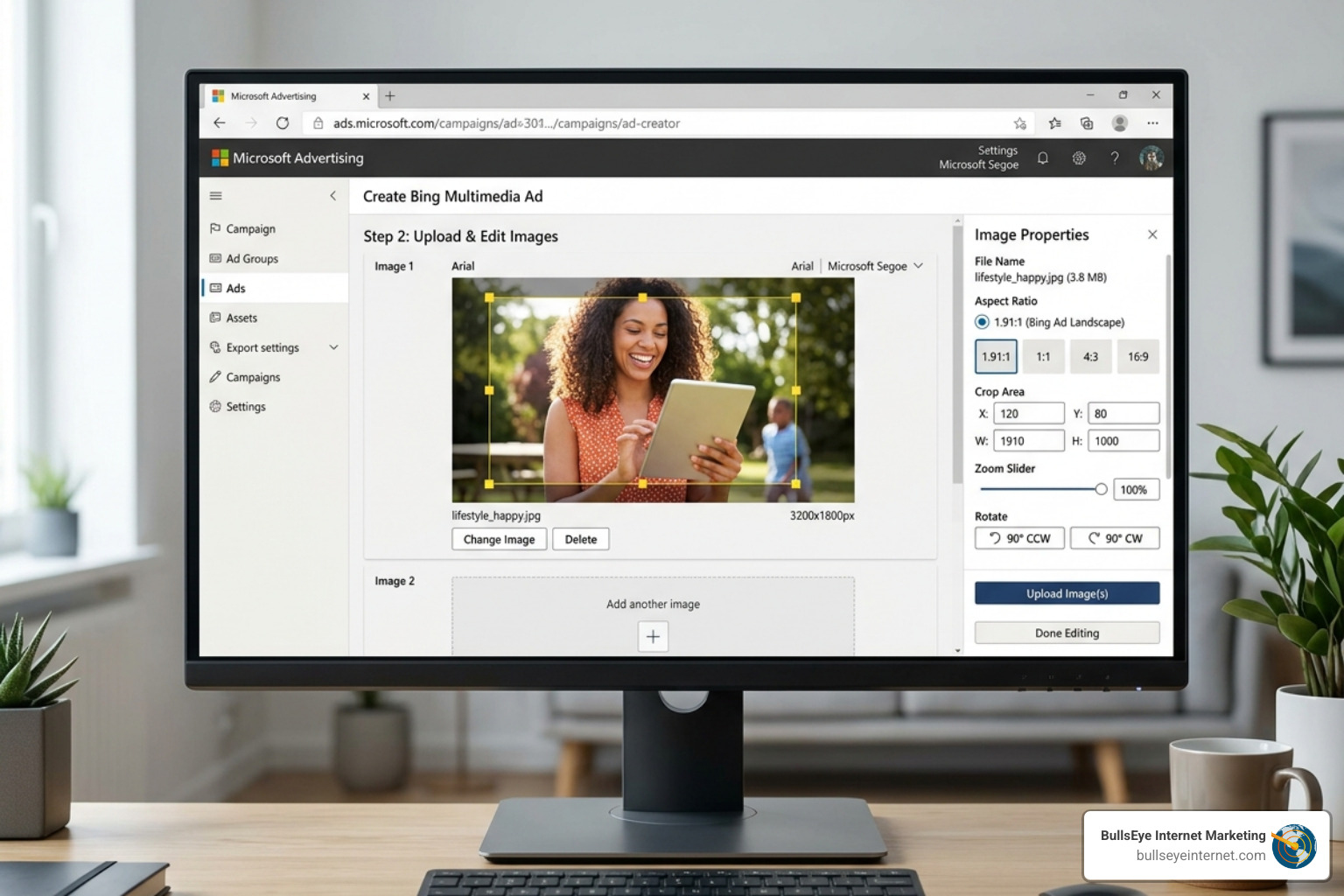 Person smiling while editing a Bing Multimedia Ad on a computer, showcasing the image upload interface with a tablet in hand, emphasizing professional ad creation and digital marketing strategies.
